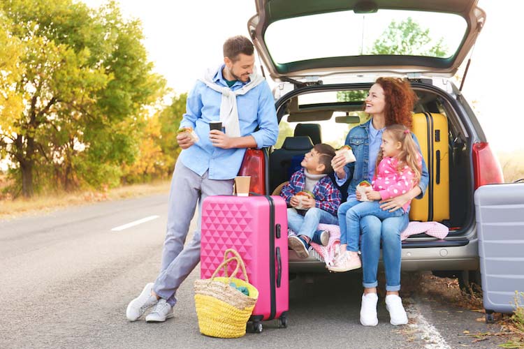 traveling family enjoying healthy travel snacks outside of their car